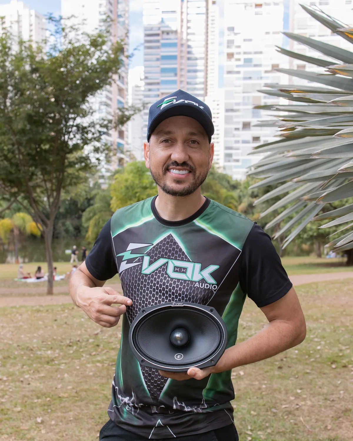 Representante da Evok Áudio segurando um alto-falante na rua, com prédios ao fundo.